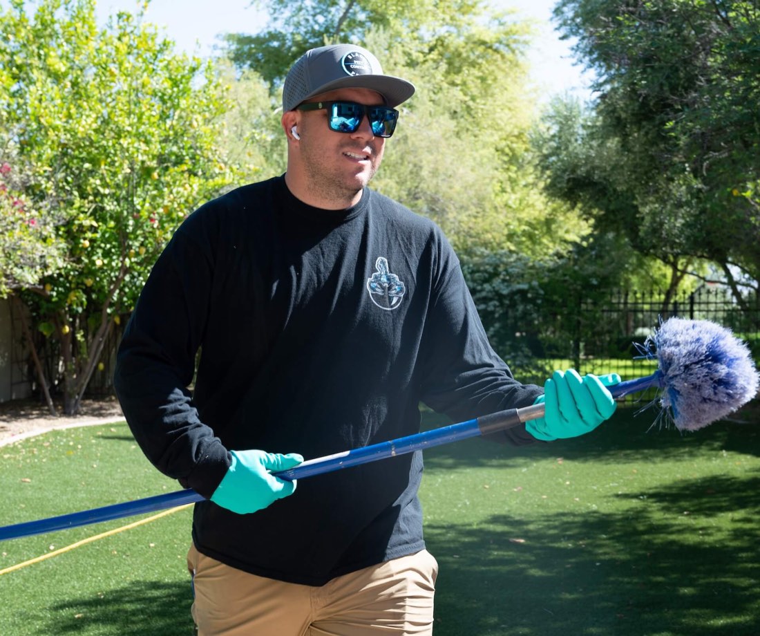 A Black Pearl Pest Control technician clearing webs from the eaves of an Arizona backyard