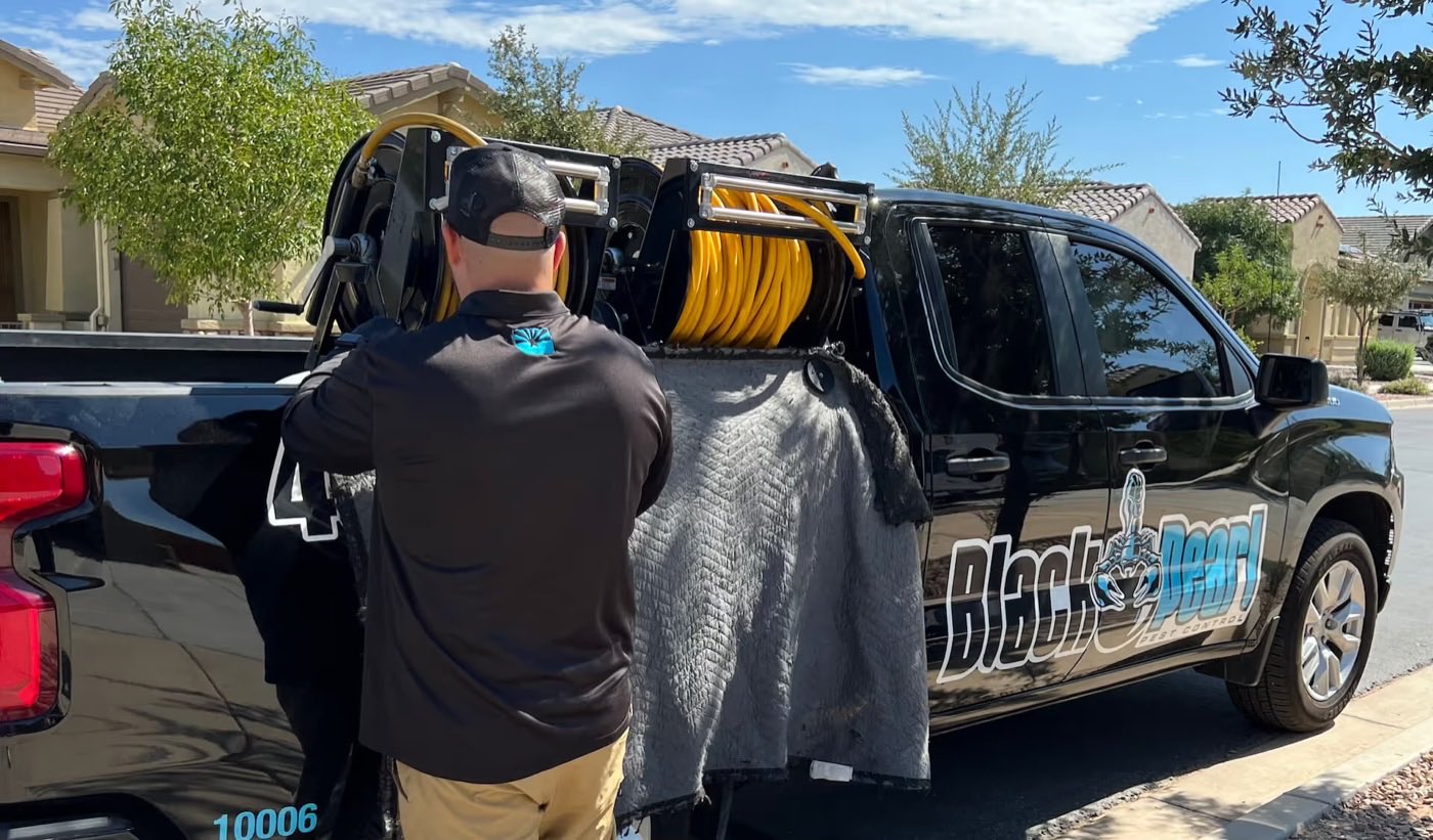 A Black Pearl Pest Control technician unloading equipment from a branded service truck outside an Arizona home